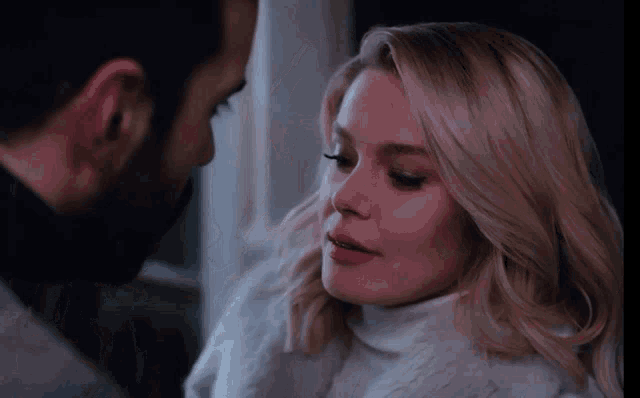 a man and a woman are looking at each other and the woman is wearing a white turtleneck