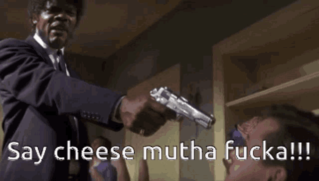a man in a suit and tie is pointing a gun at another man with the words say cheese mutha fucka