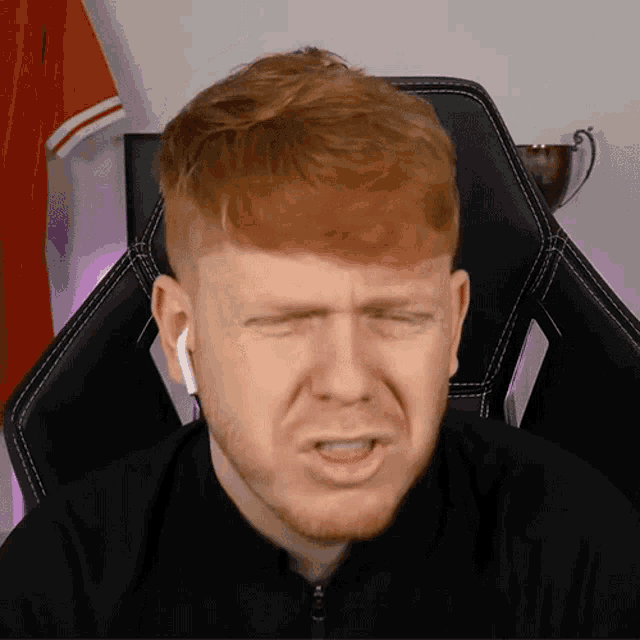 a man with red hair and a beard is sitting in a chair and making a funny face