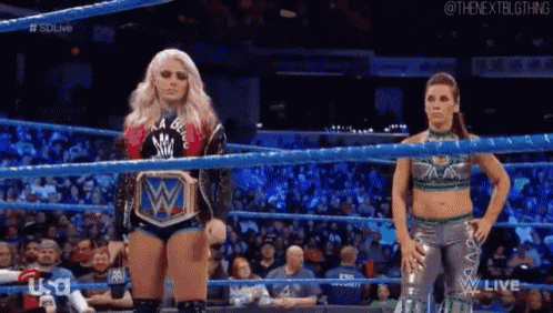 two female wrestlers are standing in a wrestling ring looking at each other .