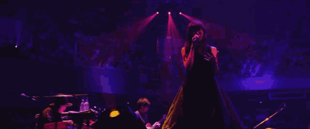 a woman singing into a microphone on a stage with purple lights
