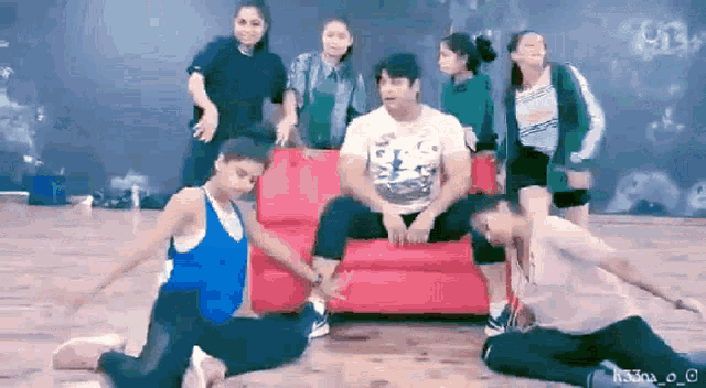 a group of people are dancing in front of a man sitting on a couch