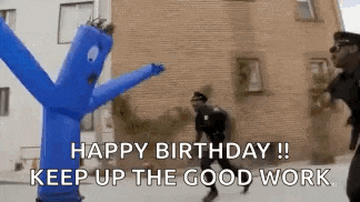 a man in a police uniform is dancing in front of a blue inflatable man .