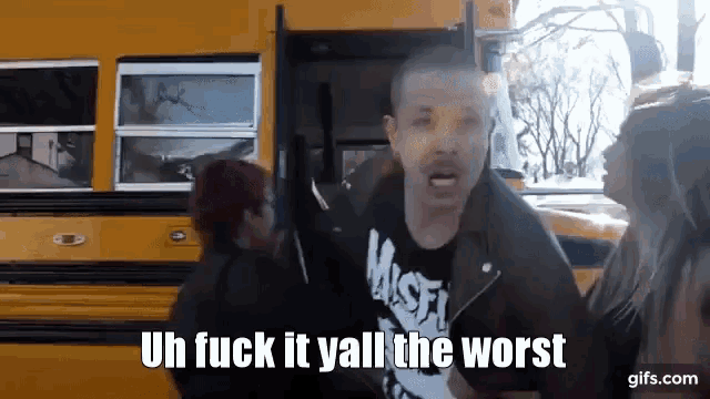 a man in a misfits shirt is standing in front of a school bus .