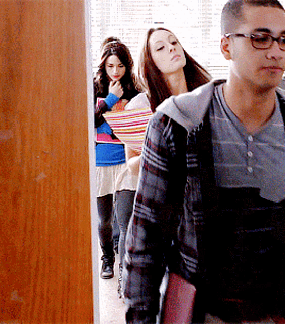 a man wearing glasses and a plaid shirt is walking with two women