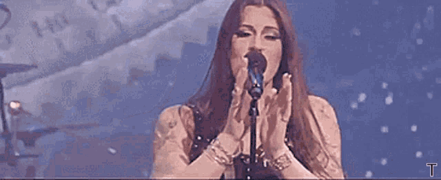 a woman is singing into a microphone with her arms outstretched on a stage .