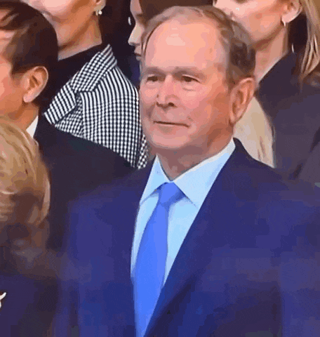 a man in a blue suit and blue tie is standing in front of a crowd of people .