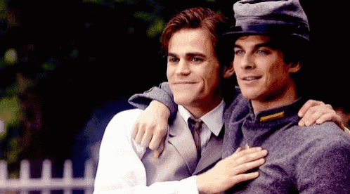 a man in a hat is hugging another man in a suit and tie .