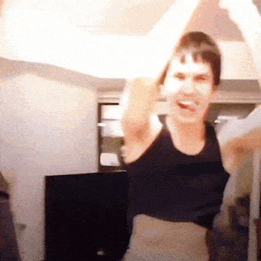 a man in a black tank top is dancing in a living room