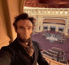 a man with a beard takes a selfie in front of a building