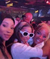 three women wearing sunglasses pose for a picture in a crowded room
