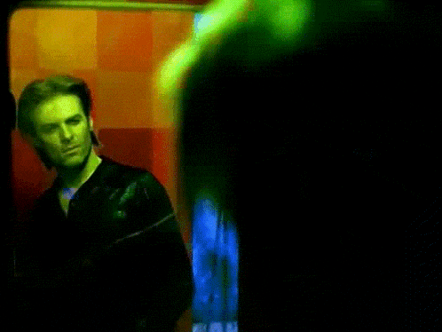 a man in a black jacket is standing in front of a red wall