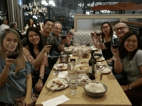 a group of people are sitting at a table holding wine glasses and smiling