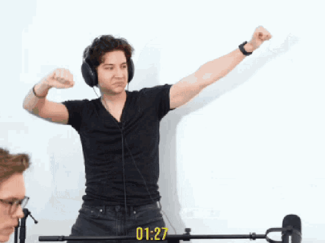 a man wearing headphones stands in front of a microphone with the time 01:25
