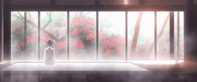 a woman sits in front of a large window with pink flowers in the background ..