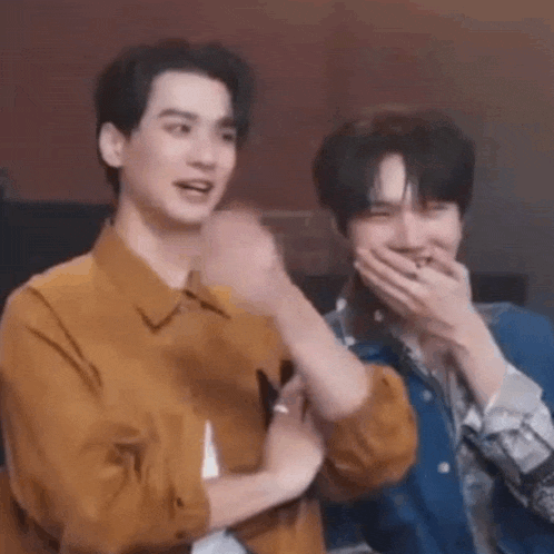 two men are sitting next to each other laughing and covering their mouths .