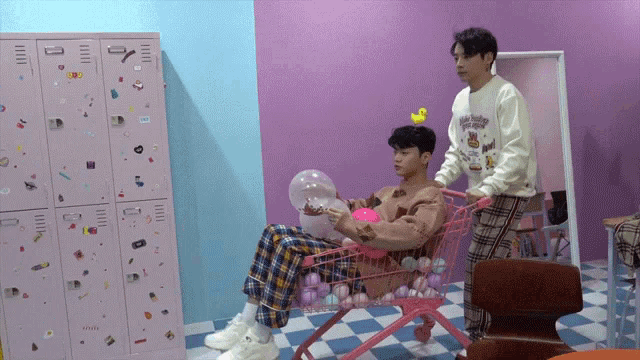 a man is pushing a pink cart full of balls while another man sits in it