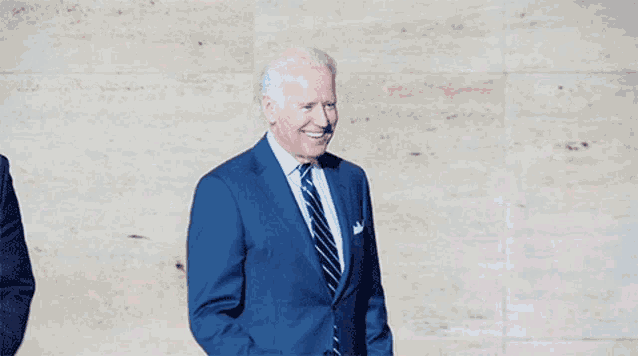 a man in a suit and tie is standing in front of a wall with his fist in the air .