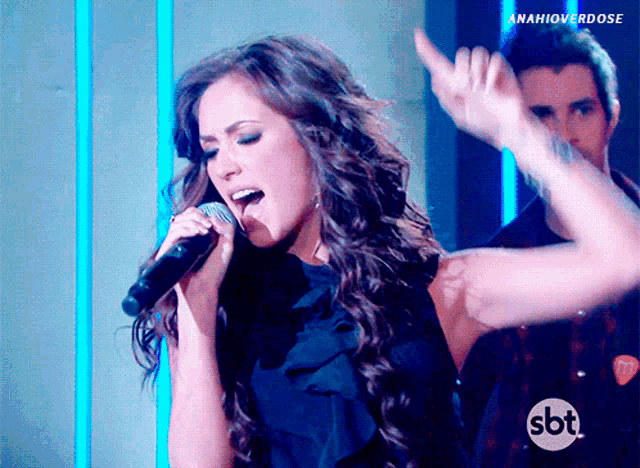 a woman singing into a microphone with the sbt logo in the corner