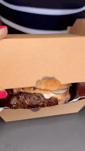 a person with pink nails is holding a hamburger in a box