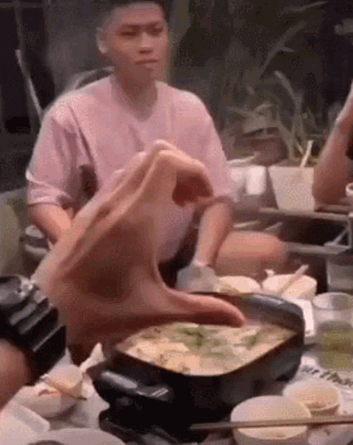 a man in a pink shirt is sitting at a table with chopsticks and a bowl of food .
