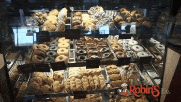a variety of donuts and pastries are displayed in a robin 's bakery case