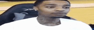 a man in a white shirt is sitting in a chair on a basketball court and looking at the camera .