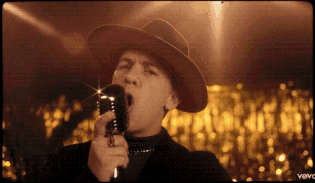 a man in a red hat singing into a microphone with the word vevo on the bottom right