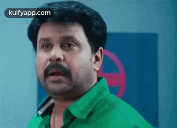 a man with a mustache is wearing a green shirt and making a surprised face .
