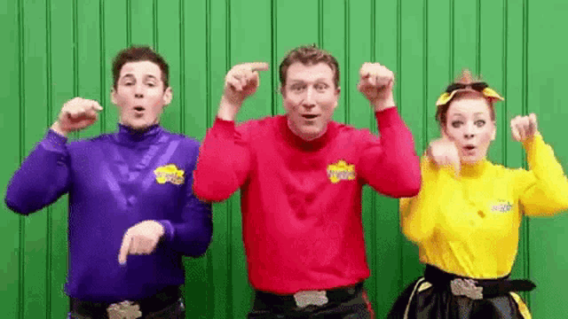a group of people are standing next to each other in front of a green wall and dancing .