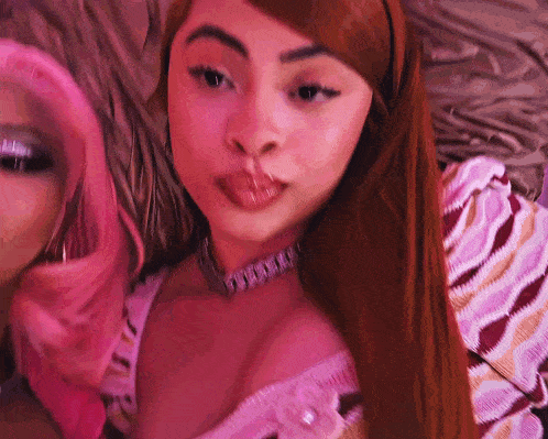 two women with pink hair are laying on a bed and one is wearing a choker .