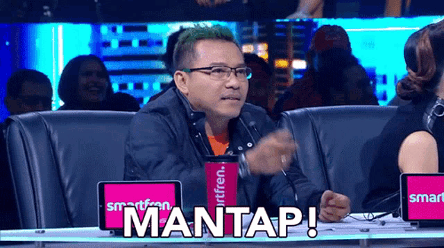 a man with green hair is sitting in front of a sign that says mantap on it