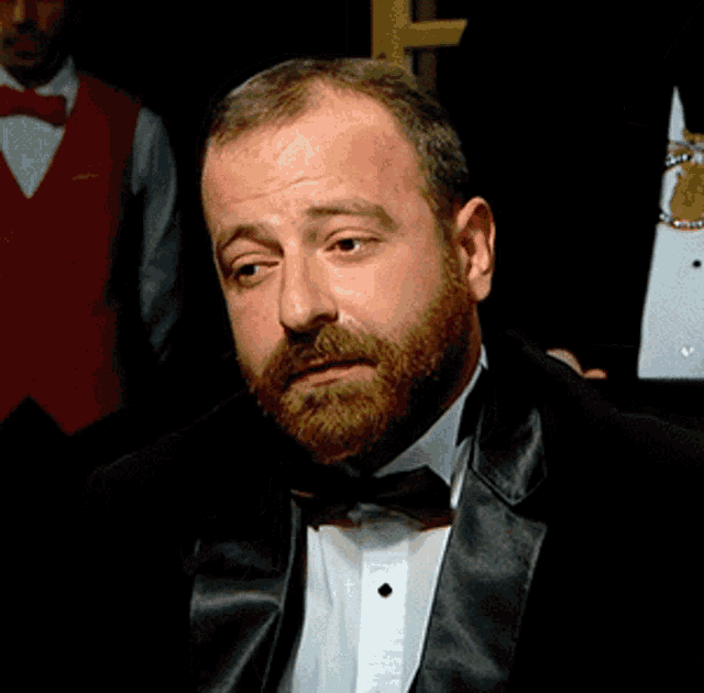 a man with a beard is wearing a black tuxedo