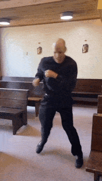 a man in a black shirt is dancing in a church with wooden benches
