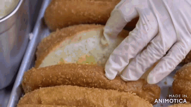 a person wearing gloves reaches for a piece of bread on a tray of fried food