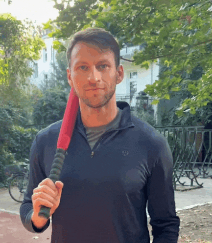 a man in a black shirt holds a red bat in his right hand