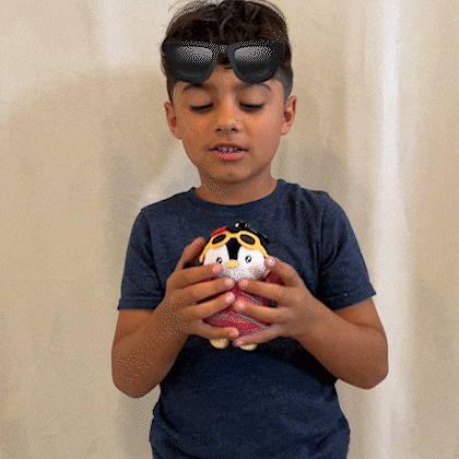 a boy wearing sunglasses holds a stuffed penguin in his hands
