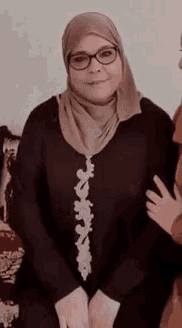 a woman in a hijab and glasses is sitting on a couch with a child .