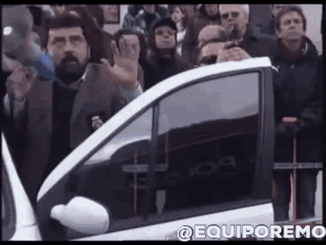 a group of people are standing around a car with the word equiporemo on the bottom of the screen .