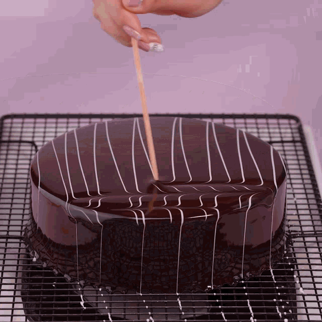 a person sticks a toothpick into a chocolate cake on a cooling rack