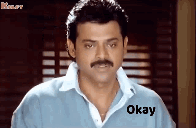 a man with a mustache is wearing a blue shirt and has the word okay written on his face .