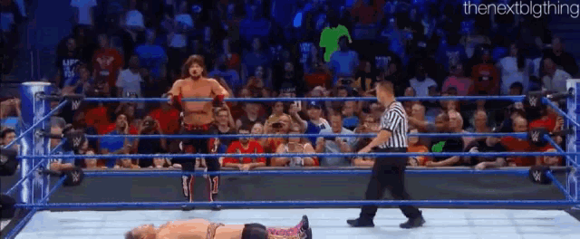 a referee is standing in the middle of a wrestling ring while a wrestler is laying on the floor .