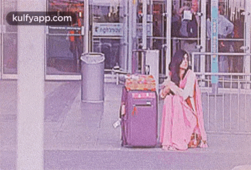 a woman in a pink sari is sitting on the ground next to a suitcase .