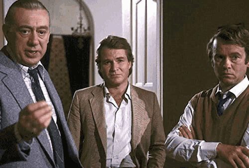 three men are standing next to each other in a room . one of the men is wearing a suit and tie .