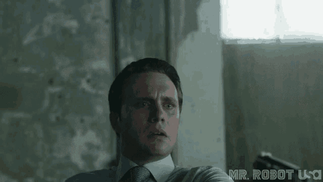 a man in a suit and tie is holding a gun in front of a window .