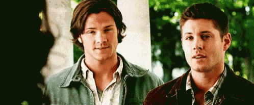 two men are standing next to each other on a porch and looking at each other .