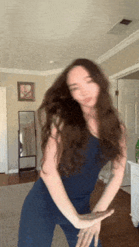 a woman in a blue top and pants is dancing in a room