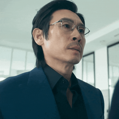 a man wearing glasses and a blue suit looks to his left