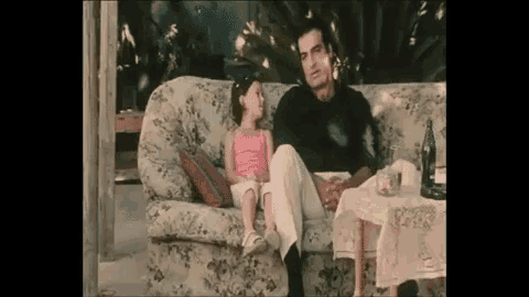 a man and a little girl are sitting on a couch . the little girl is wearing a pink top .