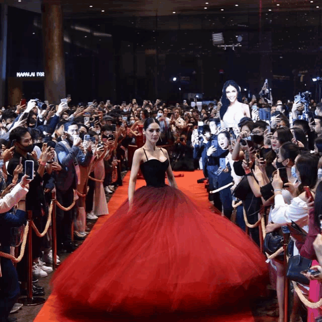a woman in a red dress is walking down a red carpet in front of a crowd of people